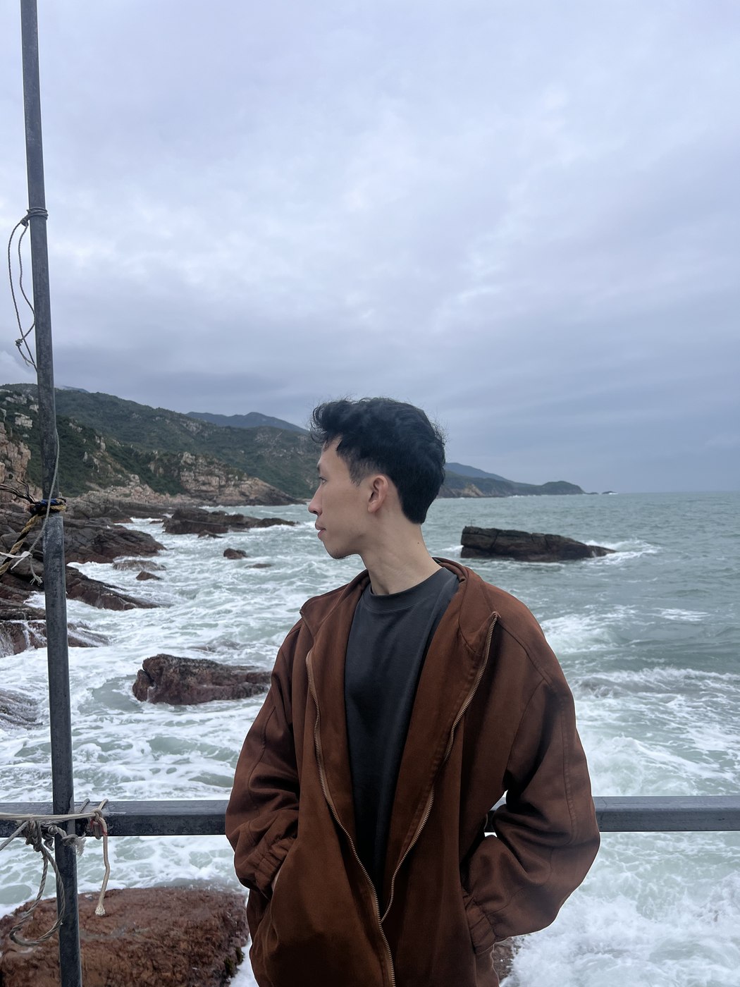 阴天的海边，穿棕色外套侧身望向远处